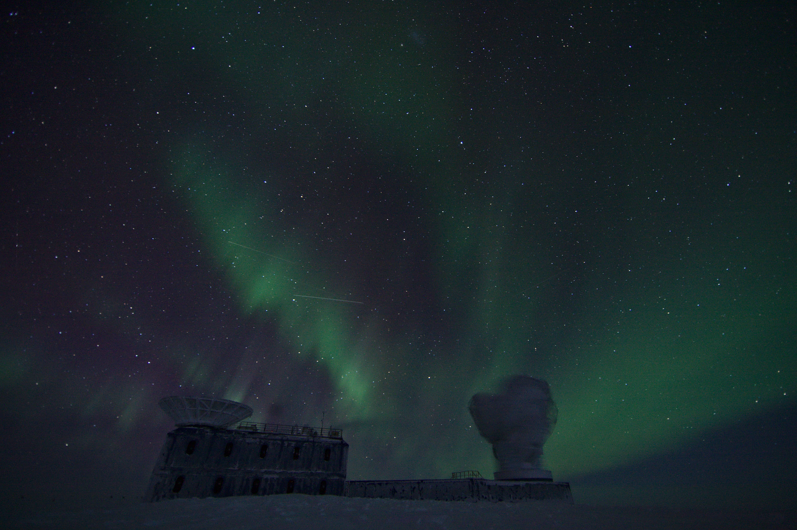 Auroras illuminate the sky while the South Pole Telescope performs CMB field observations. The Small Magellanic Cloud is visible in the very top of the picture.