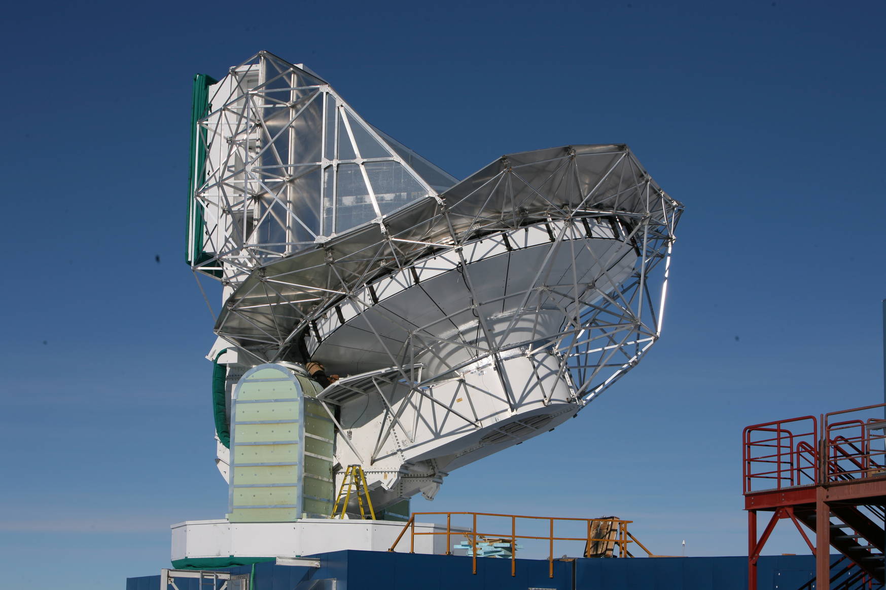 The telescope is huge! Find the person working on greasing its elevation axis for comparison. The big box in the top left (with the green bottom edge) is the receiver cabin where we will mount the new camera, once it is ready. 