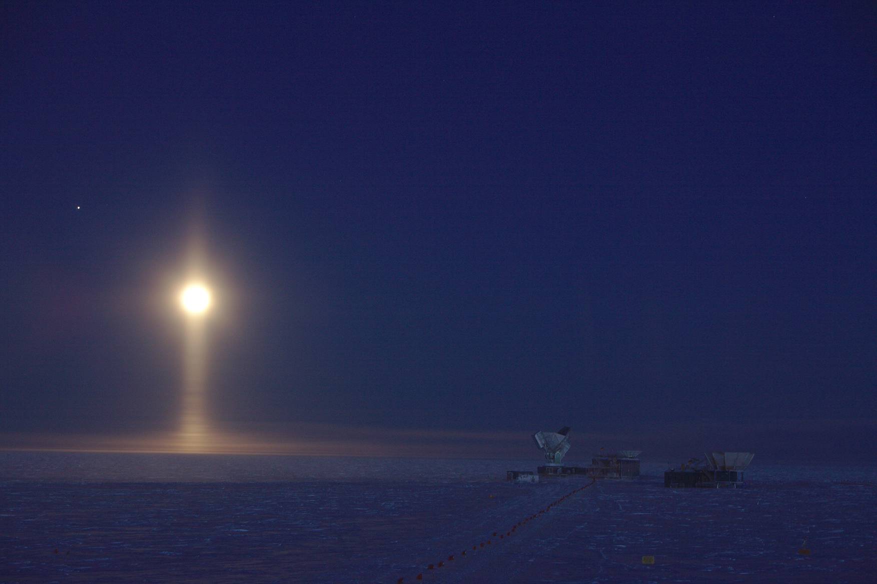 April 2017: The South Pole Telescope during EHT observations. Ice crystals in the atmosphere create a light pillar underneath the Full Moon. The bright speck left of the Moon is Jupiter.