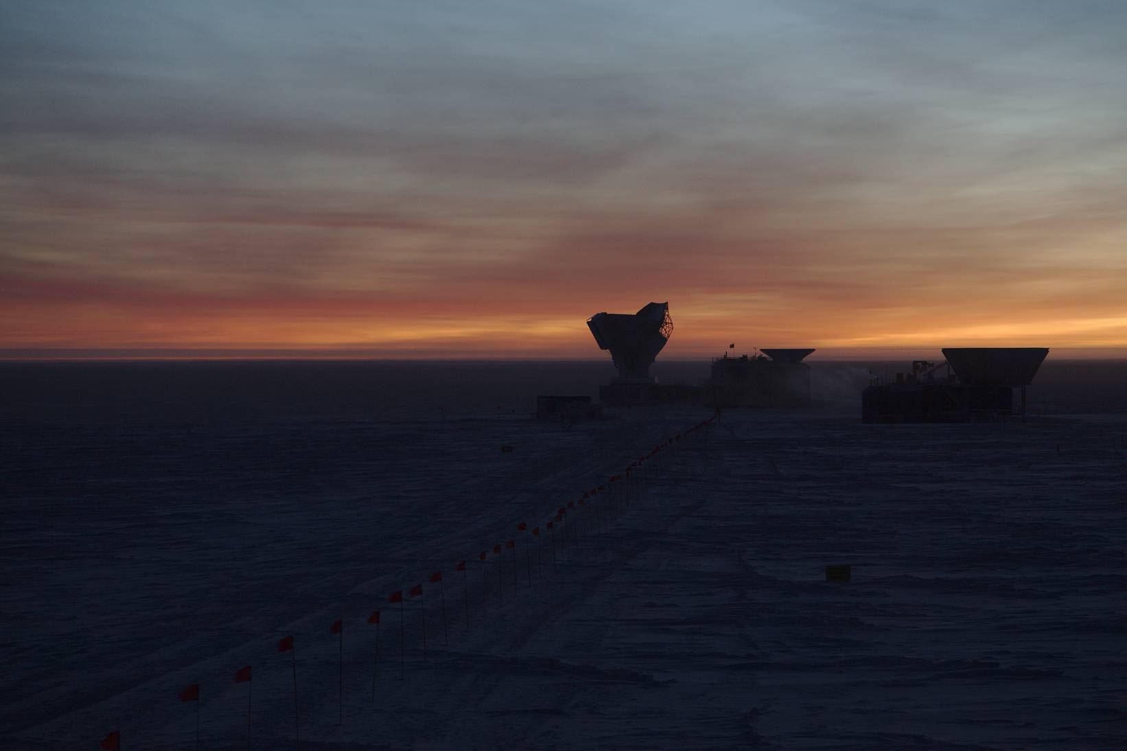 April 2017: The South Pole Telescope during EHT observations, 12 hours after the previous telescope picture. The last glimpses of the Sun behind the horizon cause the clouds in the sky to light up in hauntingly beautiful colours.